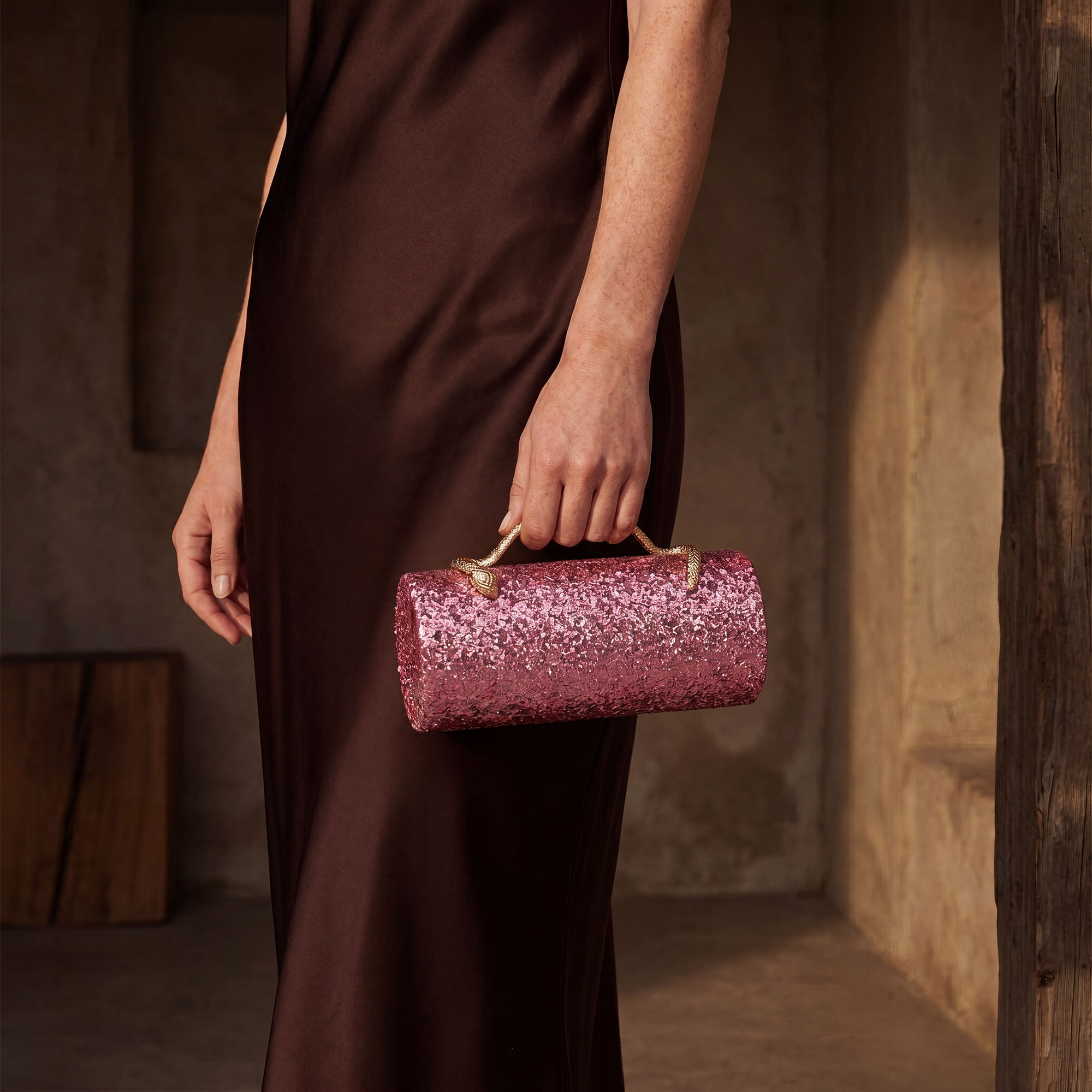 Model in brown satin dress holding Verano Hill pink glitter clutch — on-model editorial
