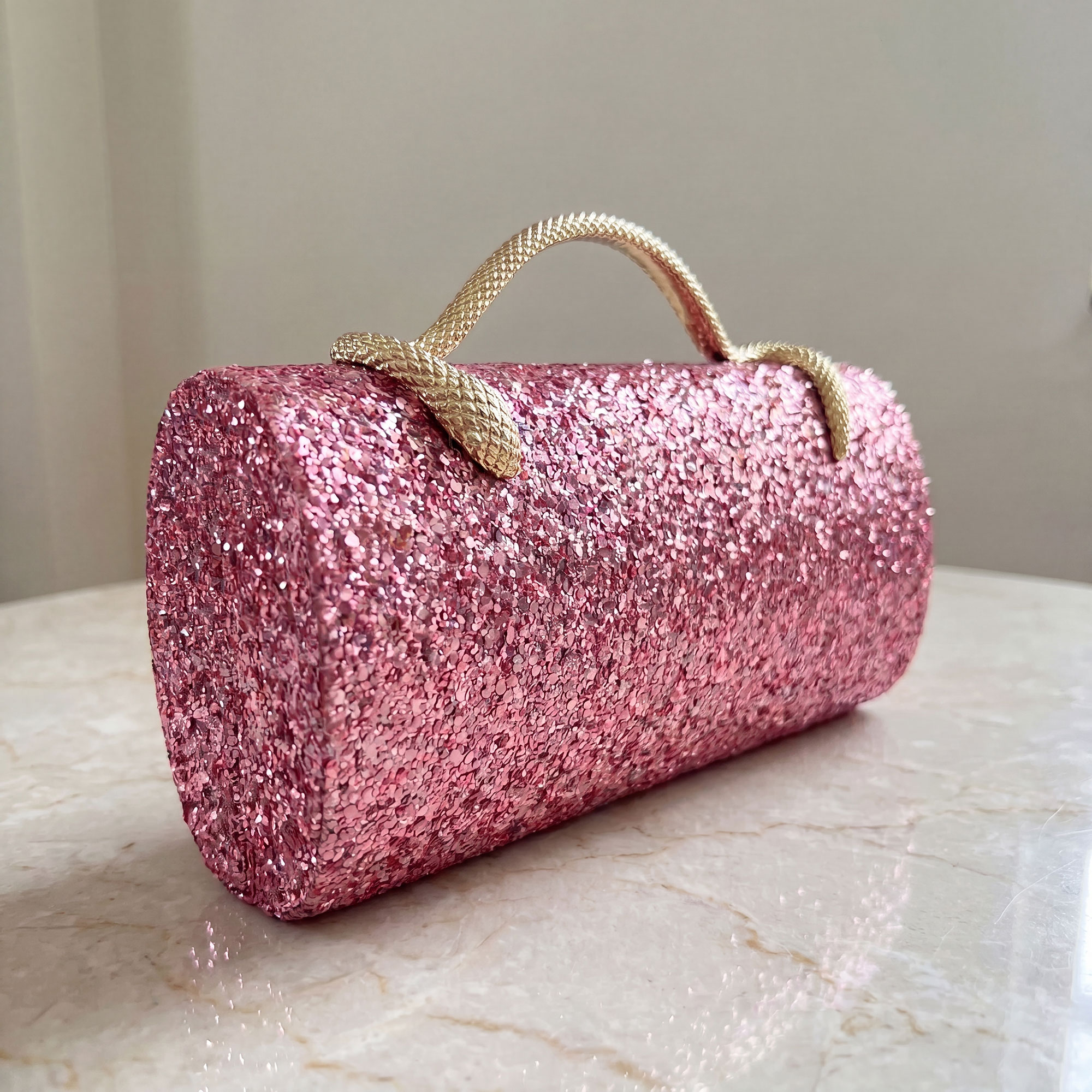 Verano Hill pink glitter clutch on a marble surface — studio packshot angle
